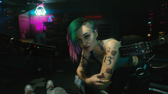 Judy leans over the player as they sit in a Braindance studio in Cyberpunk 2077.