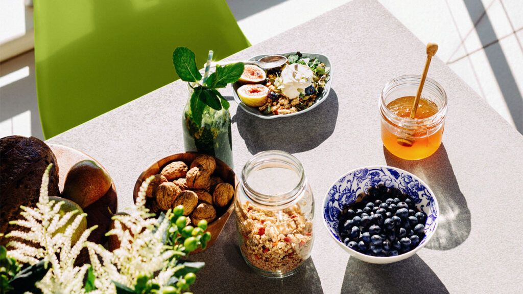 A variety of grains, fruits and vegetables on a dining table, including blueberries, honey, granola and nuts.